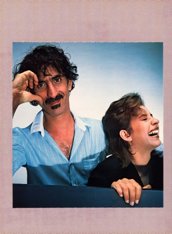 1982 photograph of Frank Zappa posing beside his laughing daughter Moon Zappa against a blue backdrop with a red-and-white patterned border.