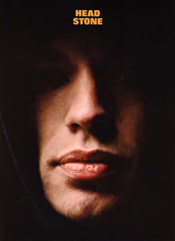 Dramatic close-up portrait of Mick Jagger with most of his face in deep shadow against a black background.